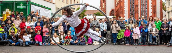 Cyr Wheel Lucky lässt modernste Zirkusdisziplin ästhethisch und mit viel Augenzwinkern aufleben, wenn er in seiner gebogenen Stahlröhre durch den Raum wirbelt.